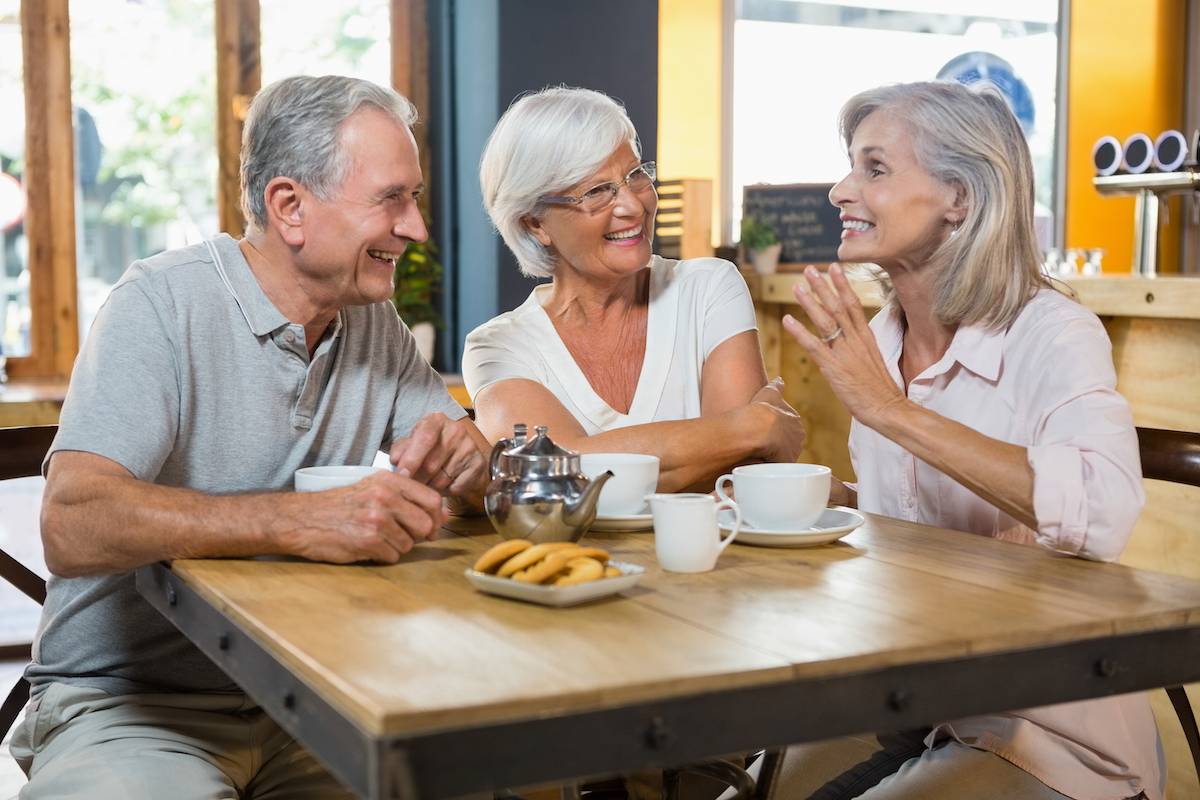 Three Older Adults Laughing Over Coffee-HarborChase Senior Living