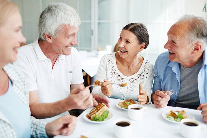 Group of Older Adults Laughing Over Coffee and Food-HarborChase Senior Living