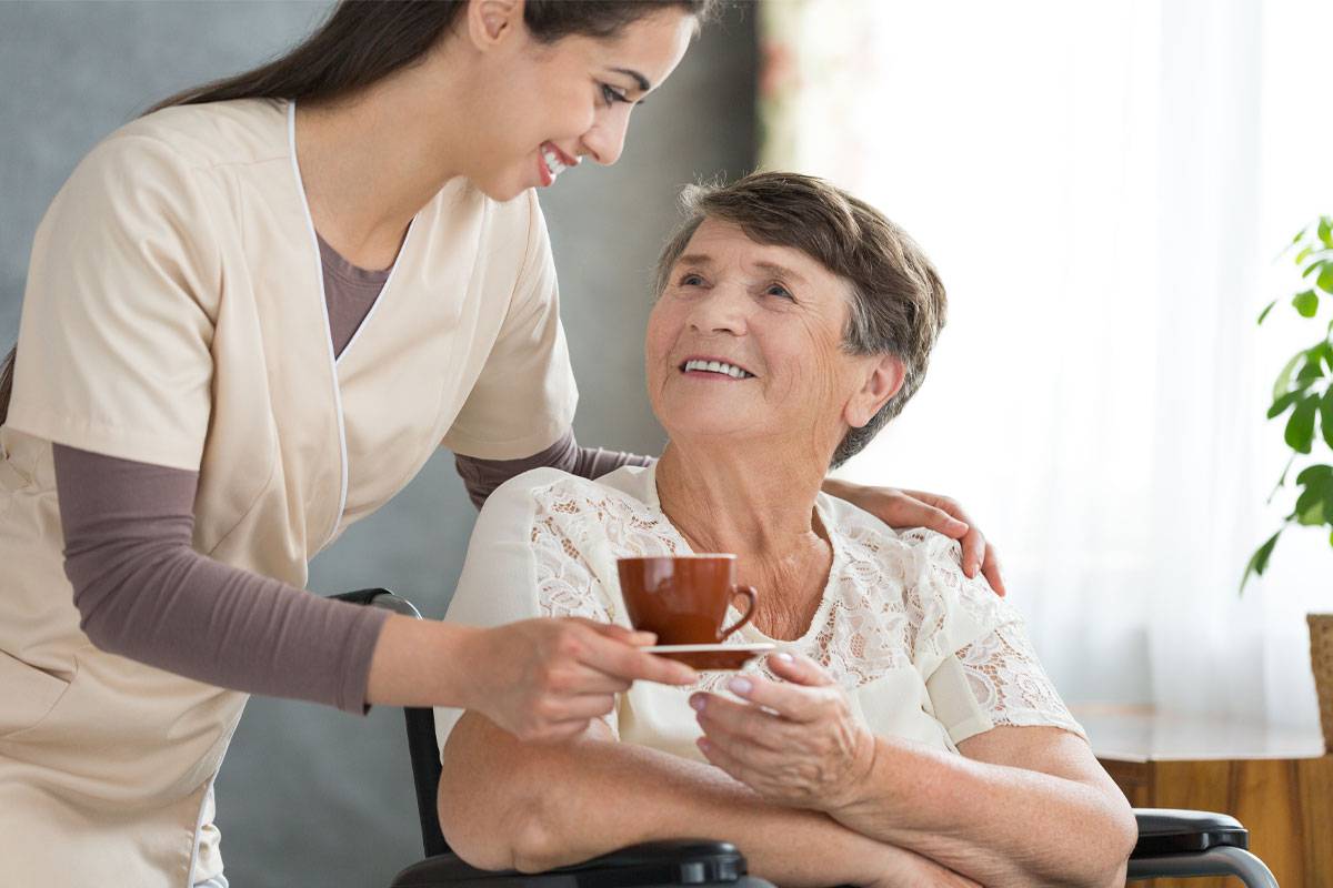 Female caregiver smiling over older woman's shoulder, handing her copy of tea