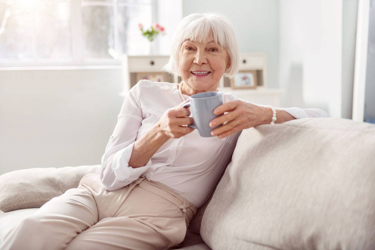 Older woman sitting on couch, holding mug and smiling