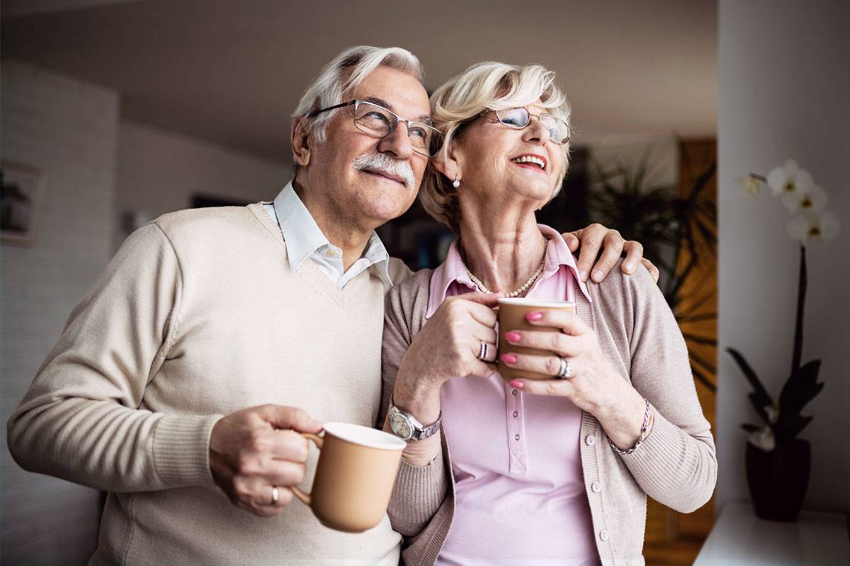 Older couple holding mugs and smiling, looking out a window