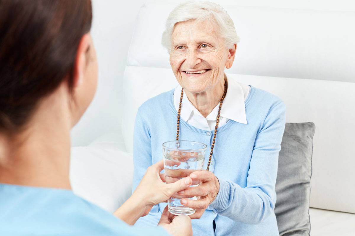 Older woman smiling, accepting glass of water from caregiver