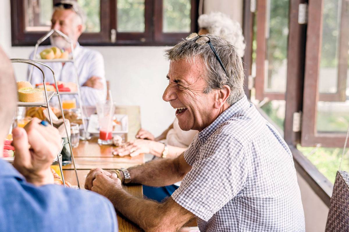 Older man laughing, sitting with friends, social opportunities
