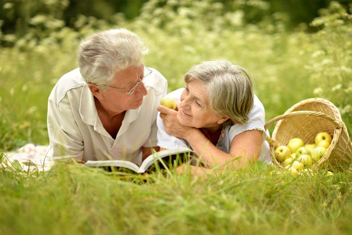 Older Couple Laying in Grass, Reading a Book-Memory Care in Palm Beach County, Florida