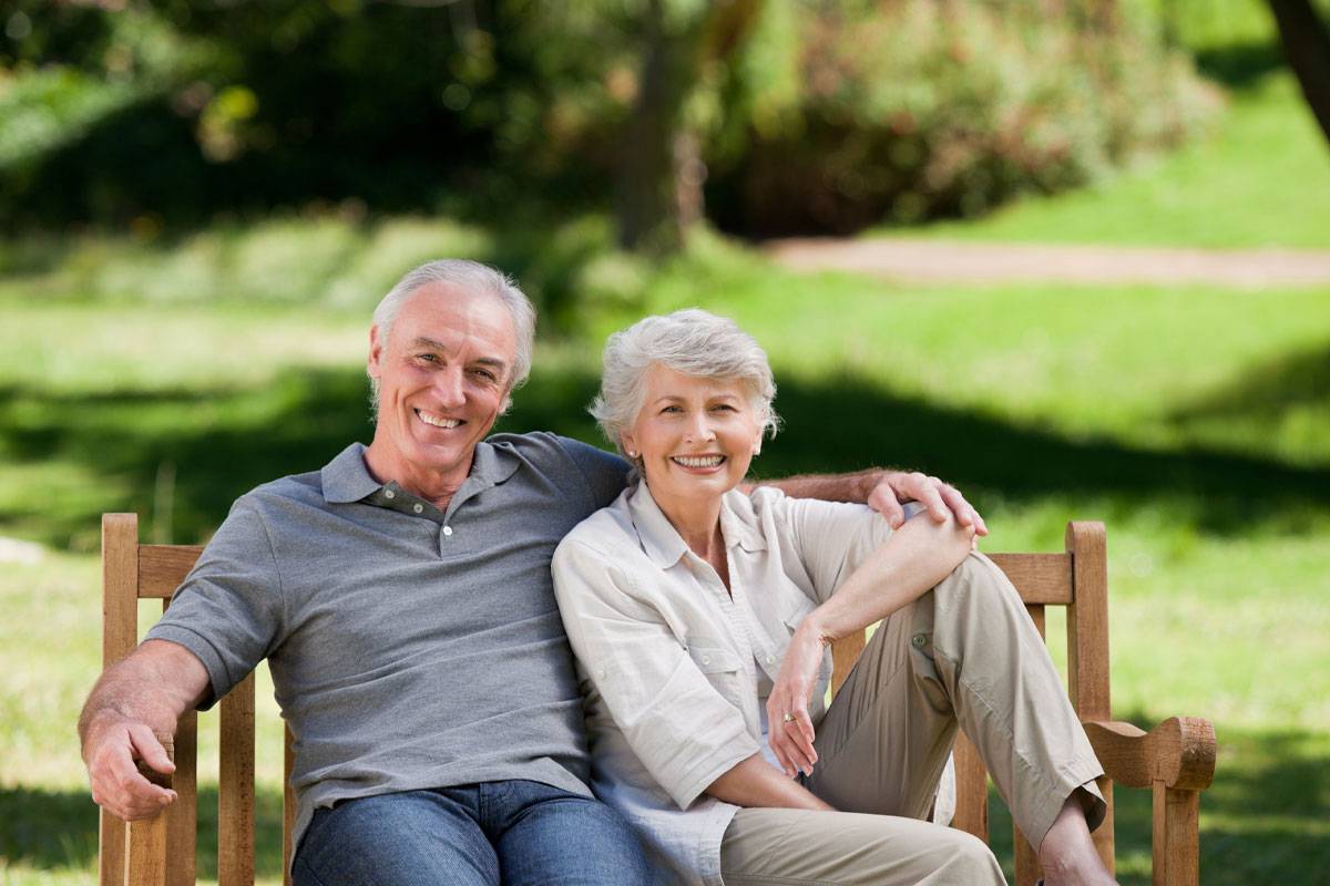 Older couple sitting on outdoor bench; smiling