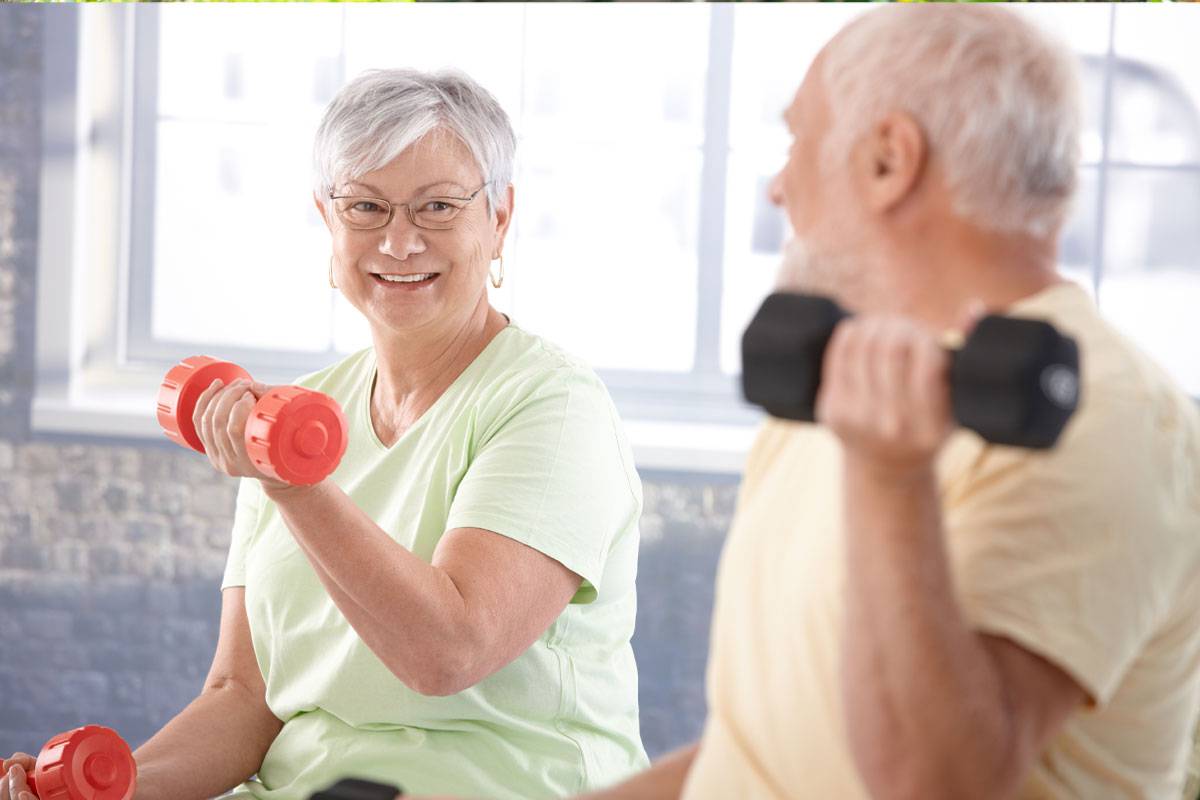 Older couple exercising with light dumbbells, looking at each other, smiling