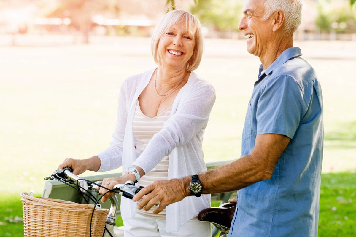 Older couple, outside, smiling; walking bicycles side by side