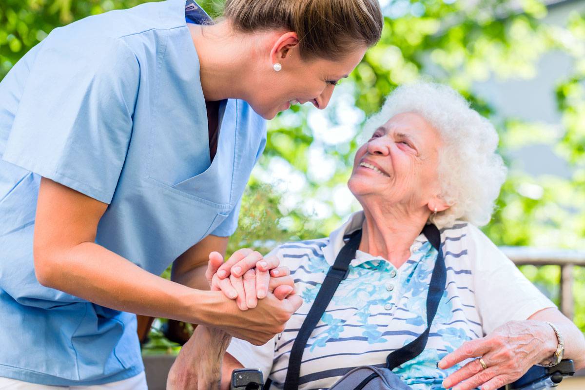 Caregiver Holding Older Woman's Hand, Smiling, Sitting Outside-Assisted Living in Palm Beach County, Florida