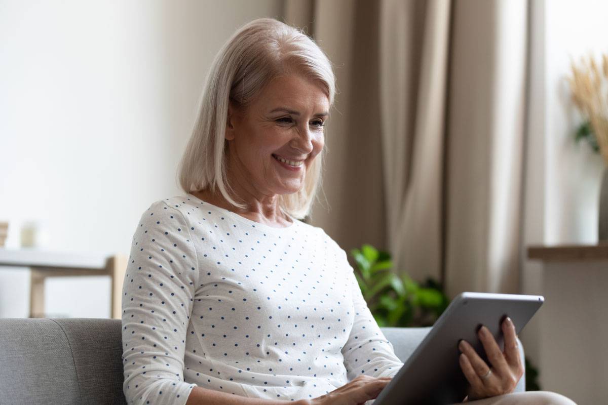 Older woman smiling, sitting on couch, looking at tablet