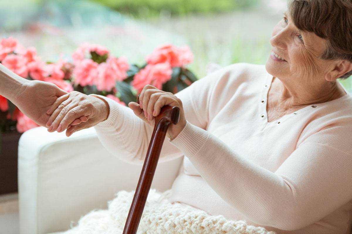 Close up of older woman with cane, holding hand of caregiver, smiling