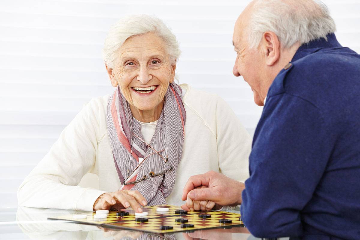 Older woman smiling; playing chess with older male