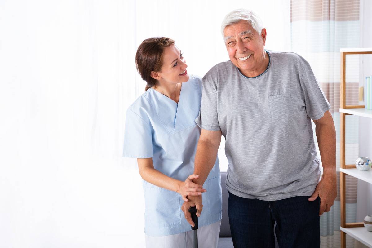 Female caregiver assisting older man with mobility, both smiling