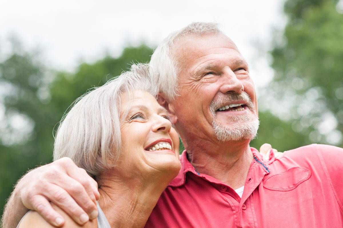 Close up of older husband and wife smiling, looking into distance, outside