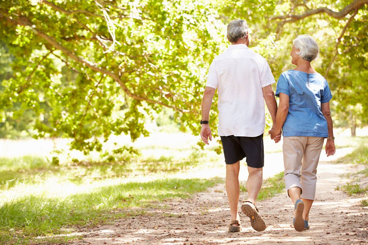 Older man and woman holding hands, walking on outdoor trail, walking away from view