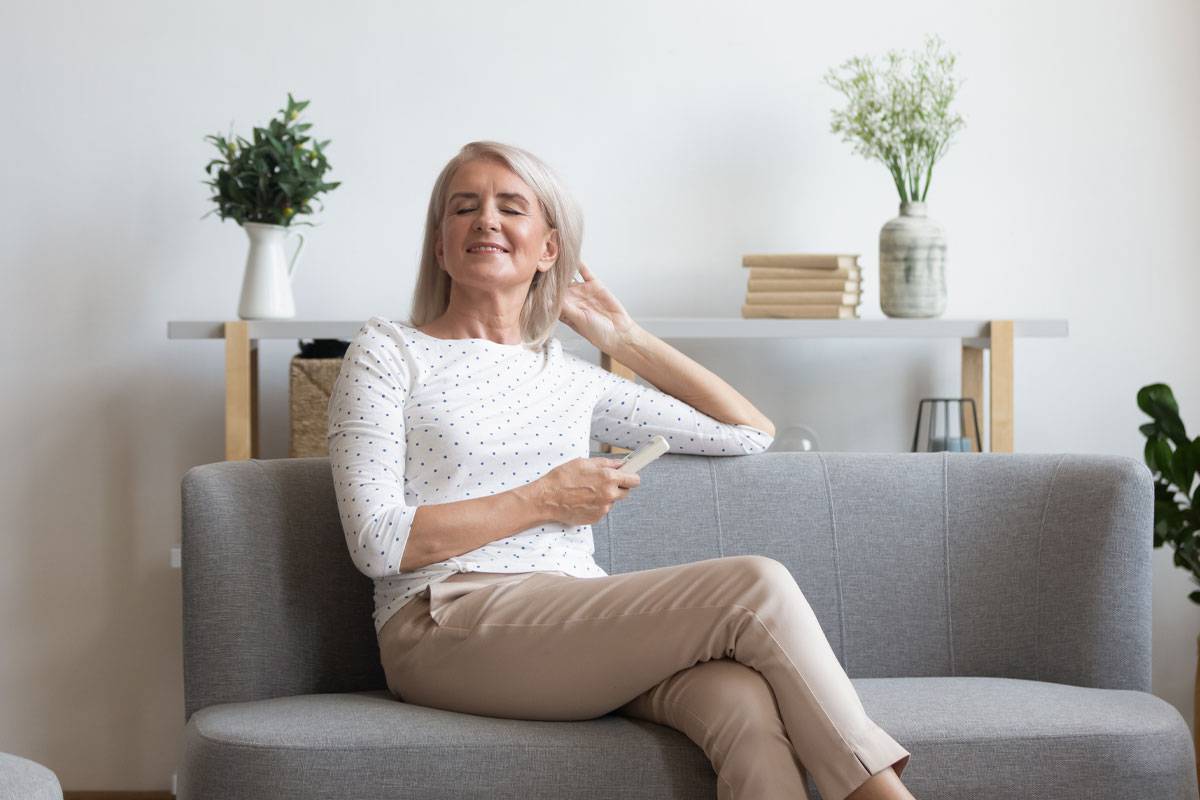 Older woman sitting on couch, smiling, holding remote