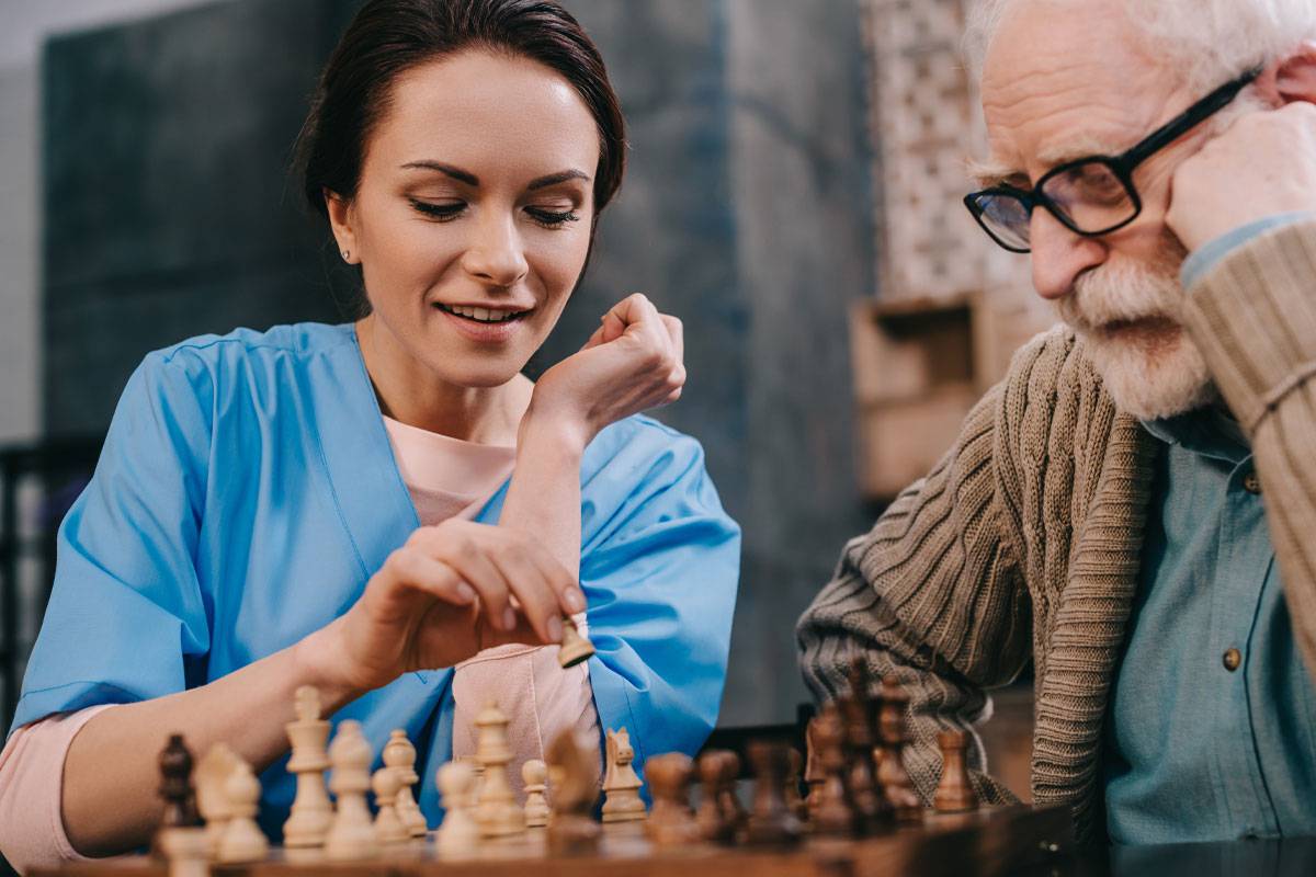 Female caregiver playing chess with older man