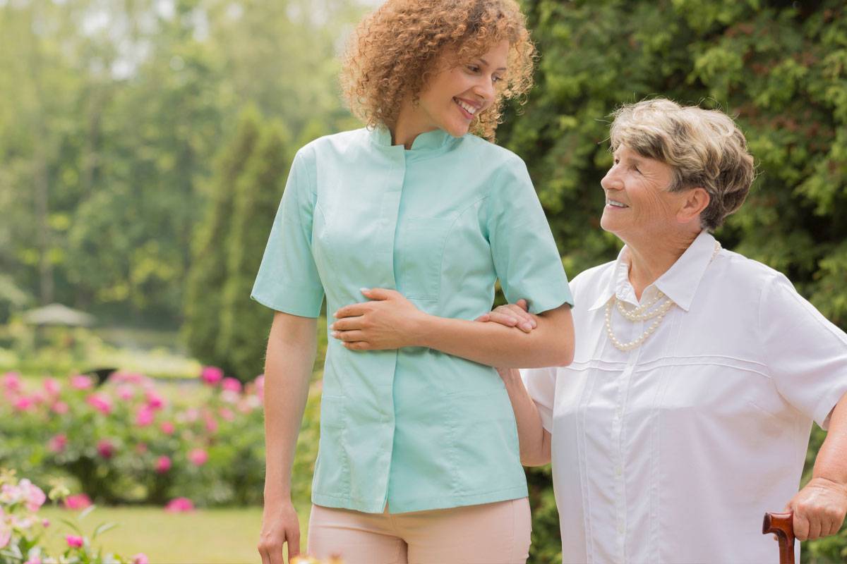 Female caregiver walking outside, arm in arm with and older woman