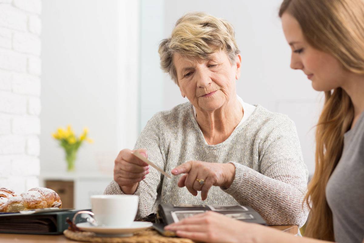 Older woman pointing to photograph, drinking tea with younger daughter