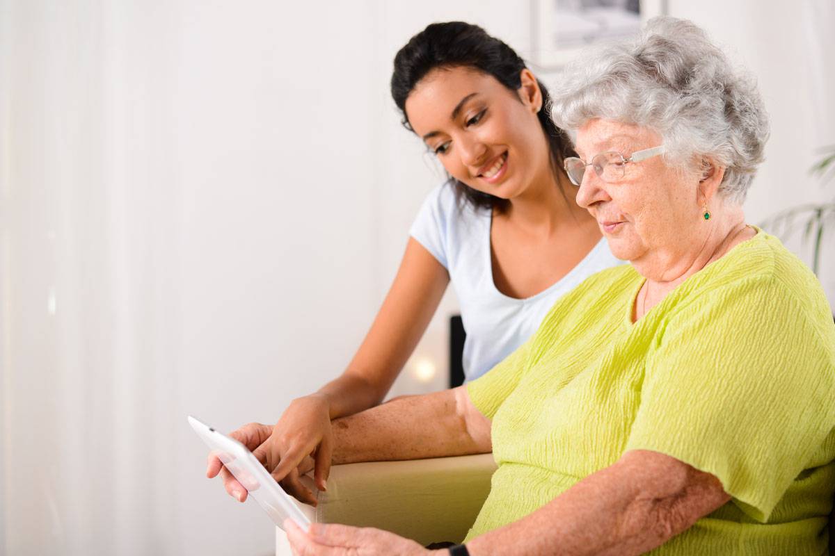 Young Woman and Older Woman Looking at Tablet-Assisted Senior Living