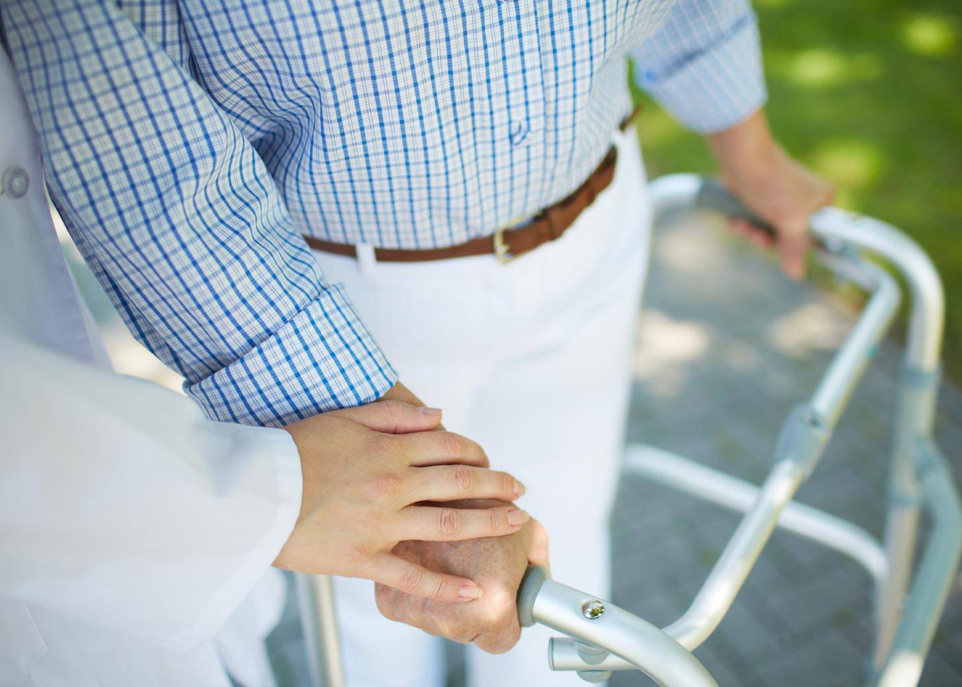 Close up of caregiver with hand on older man's hand, holding on to walking assistant