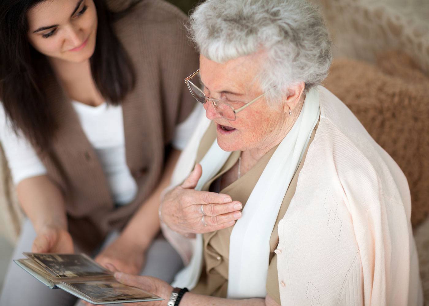 Older woman smiling, looking at photographs, younger daughter smiling next to her