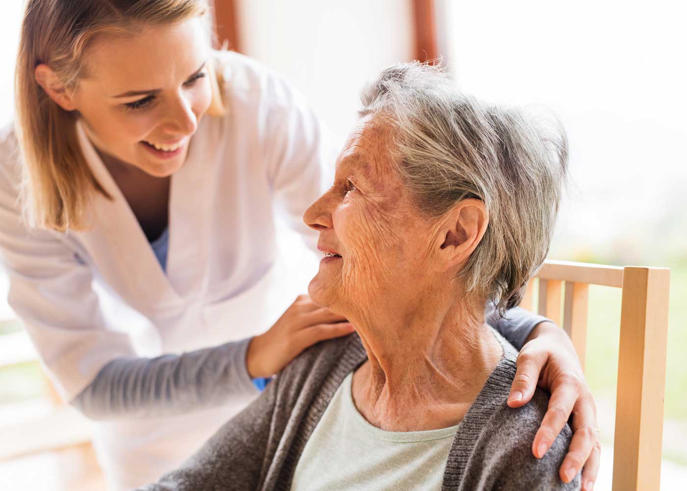 Female caregiver with both hands on older woman's shoulders; smiling at each other