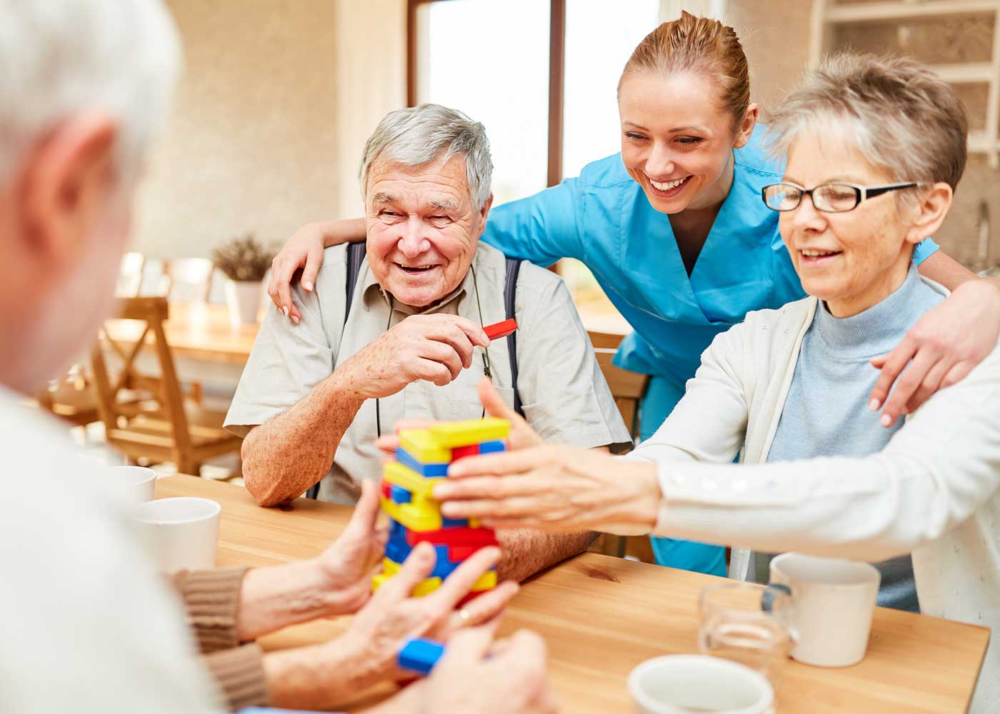 Female caregiver with arm around male resident and female residents; all smiling with playing jenga; strengthening cognitive function