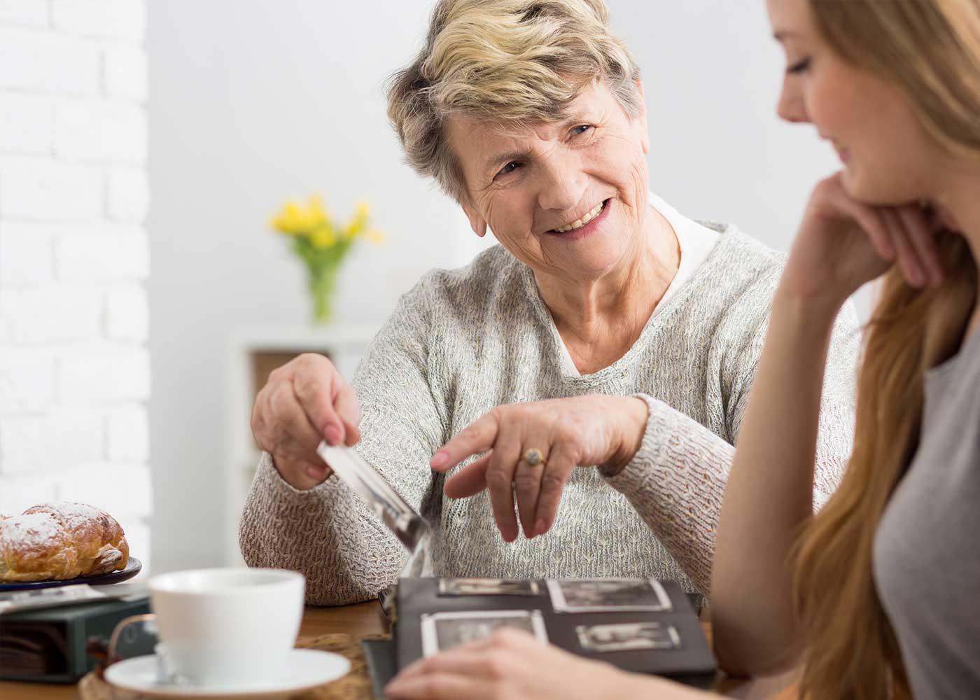 Older woman talking to daughter; showing photo and smiling; sharing coffee