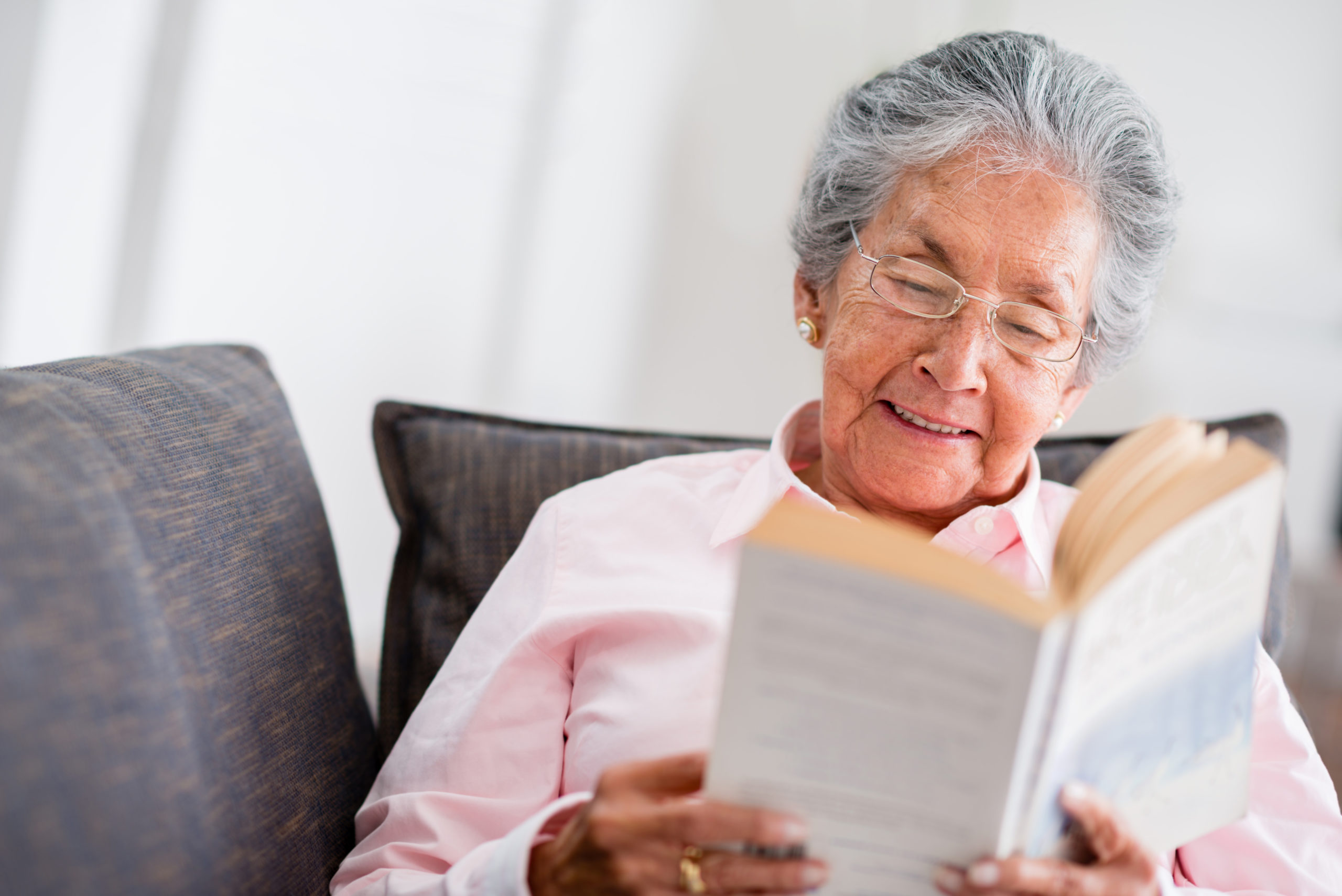Elder,Woman,Reading,A,Book,At,Home,And,Smiling
