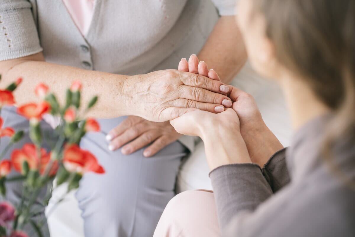 Daughter holds hands of older mother-HarborChase Memory Care