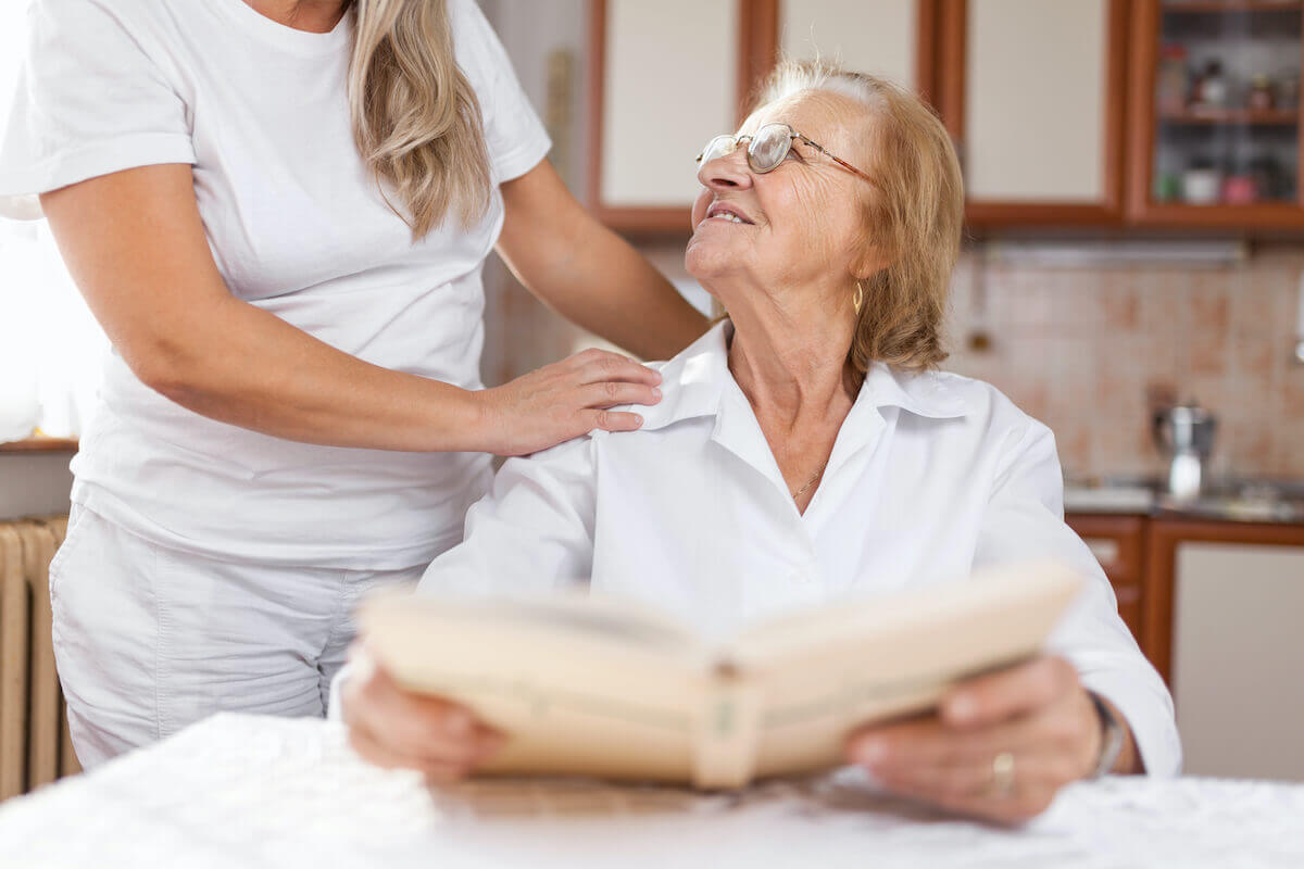 Female caregiver with hands on older woman's shoulders, reading book-Dementia Care Dos and Don'ts