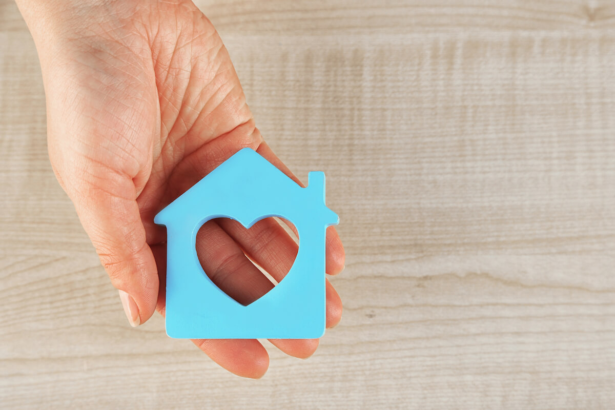 Female hand with model of house on wooden table background-Assisted living vs home care