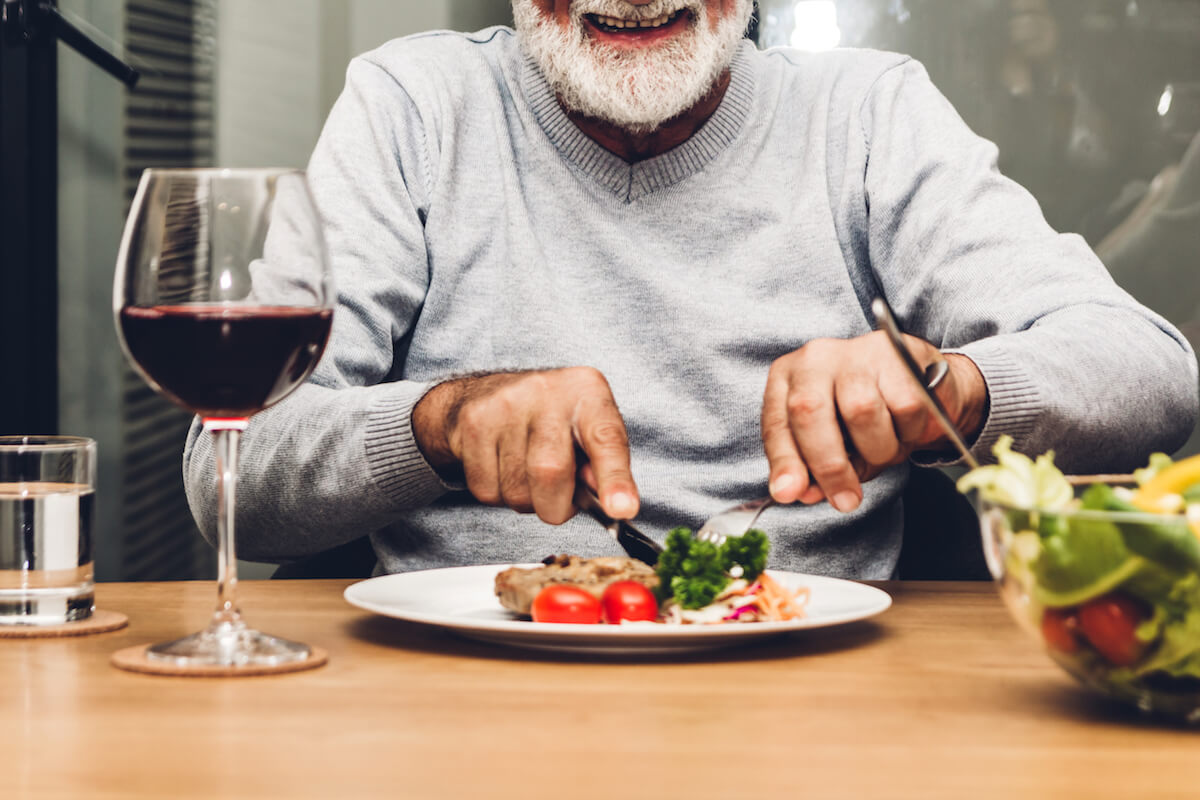 Happy senior man eating pork steak on table-Meals for one_Senior Living
