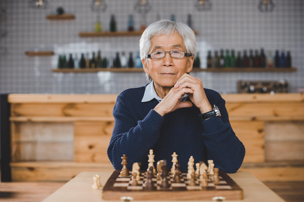 Older asian man sitting at table, chess board set up in front of him-Winter Hobbies