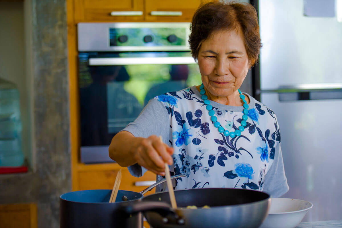 Older asian woman cooking food, standing at stove-Cooking for One