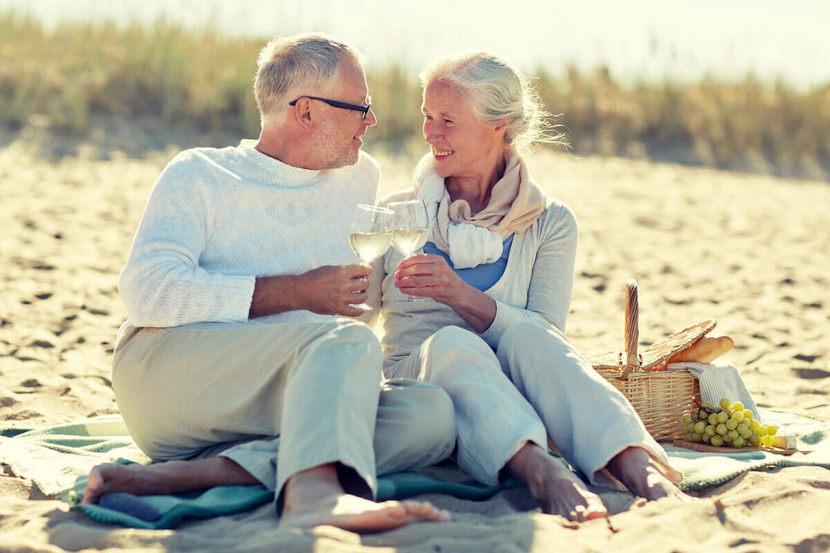 Older couple drinking wine, sitting on beach with picnic-Dating after 60