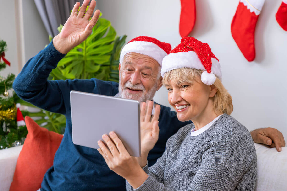 Older couple in Santa hats, waving at tablet-Honoring holiday traditions in Assisted Living