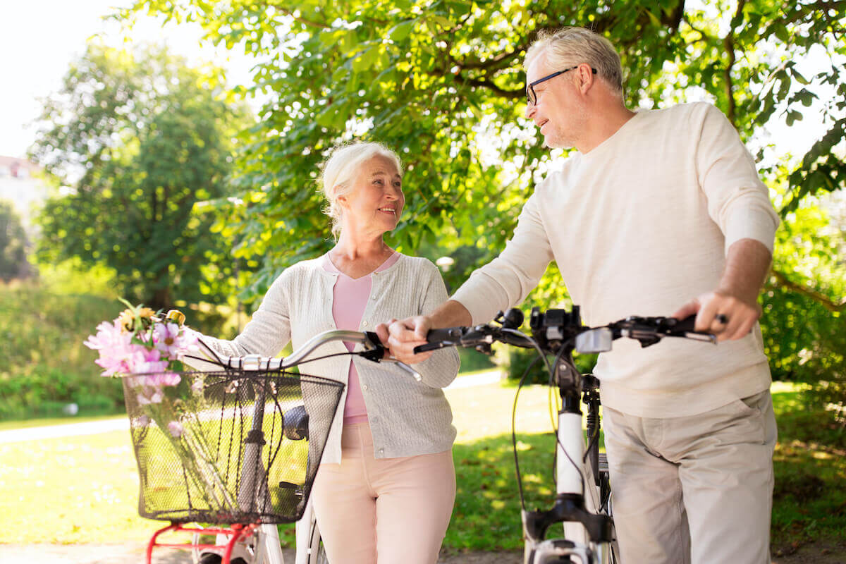 Older couple standing with bikes, outdoors, smiling-Senior Health