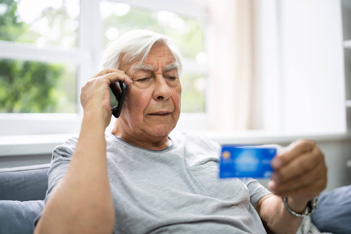 Older man on phone, reading credit card number-How to avoid COVID Scams