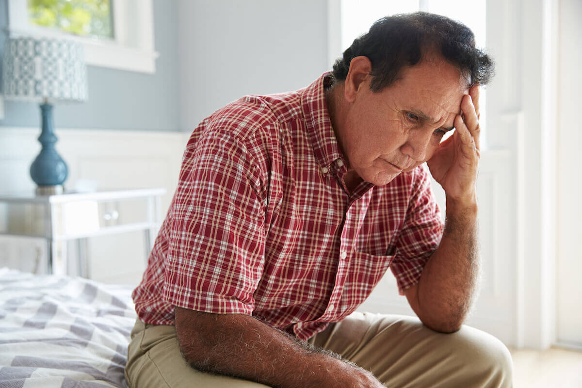 Older man sitting on edge of bed, holding head-Symptoms of Dementia