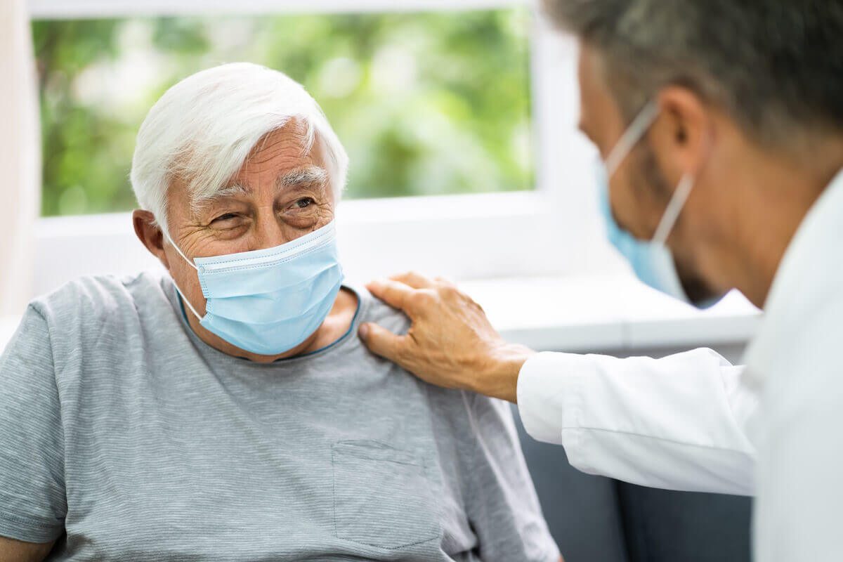 Older man wearing mask, male healthcare working with hand on shoulder-Assisted living vs nursing homes