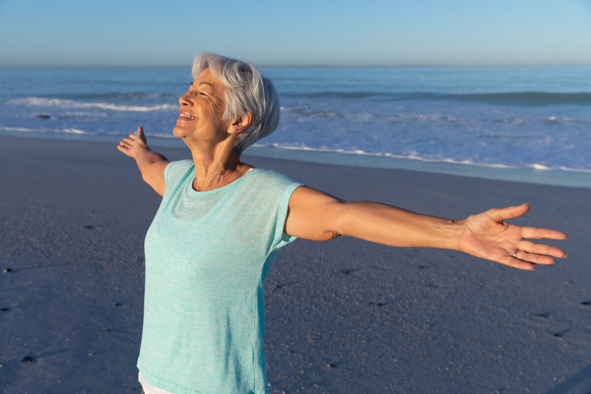Older woman arms outstretched, standing on beach-Power of positivity