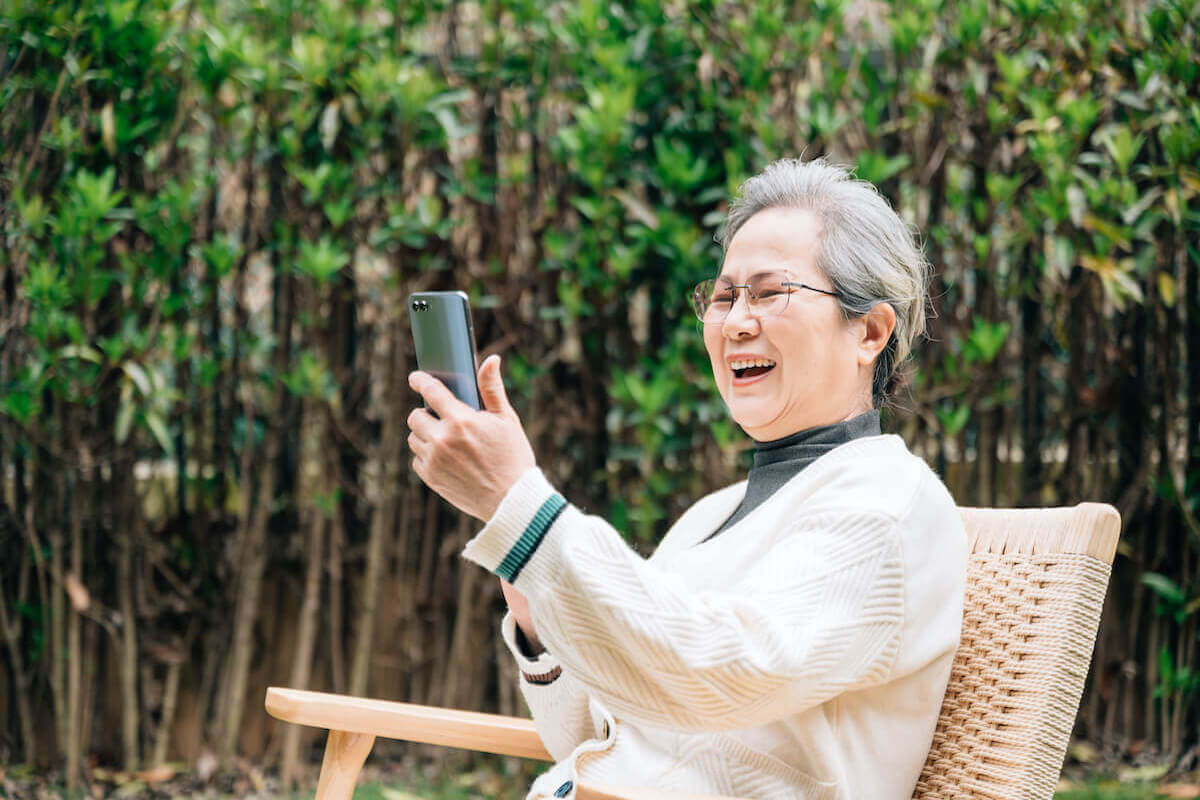 Older woman sitting outside, smiling looking at smartphone_Combatting Loneliness
