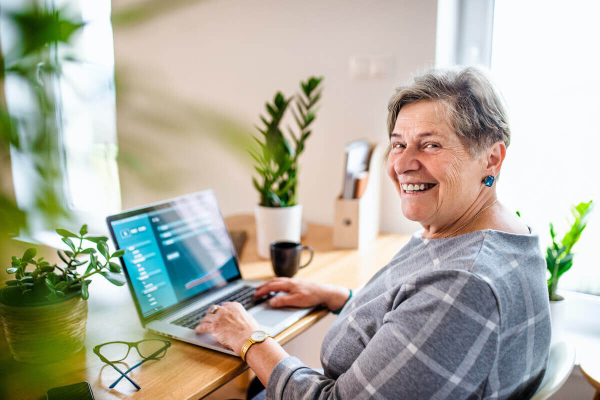 Older woman smiling, sitting at desk on laptop-Lifelong learning and continuing education