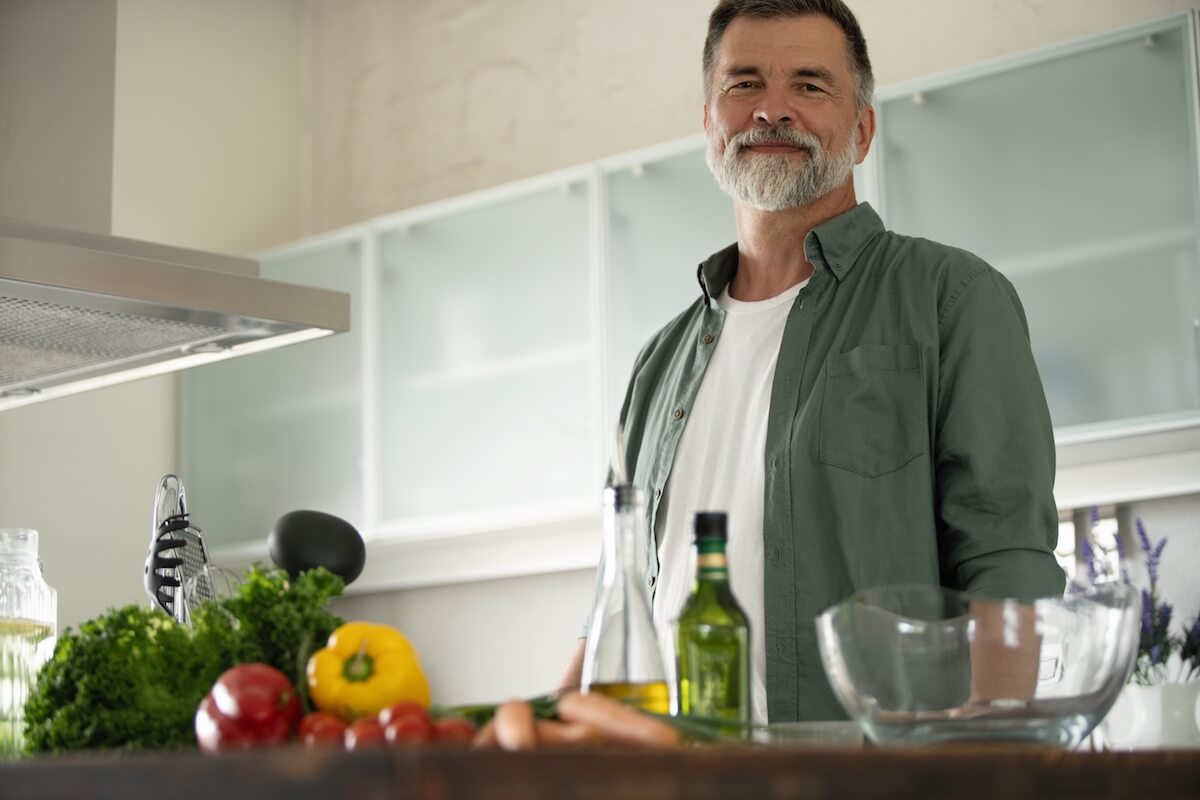 Smiling happy senior mature man standing in kitchen table-Cooking for One