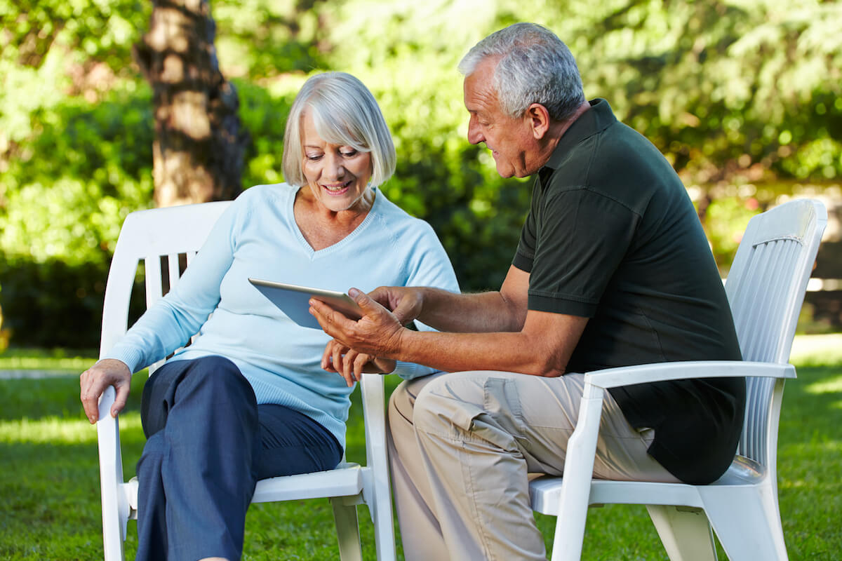 Two senior people sitting with a tablet PC in a nature park-What is Assisted Living