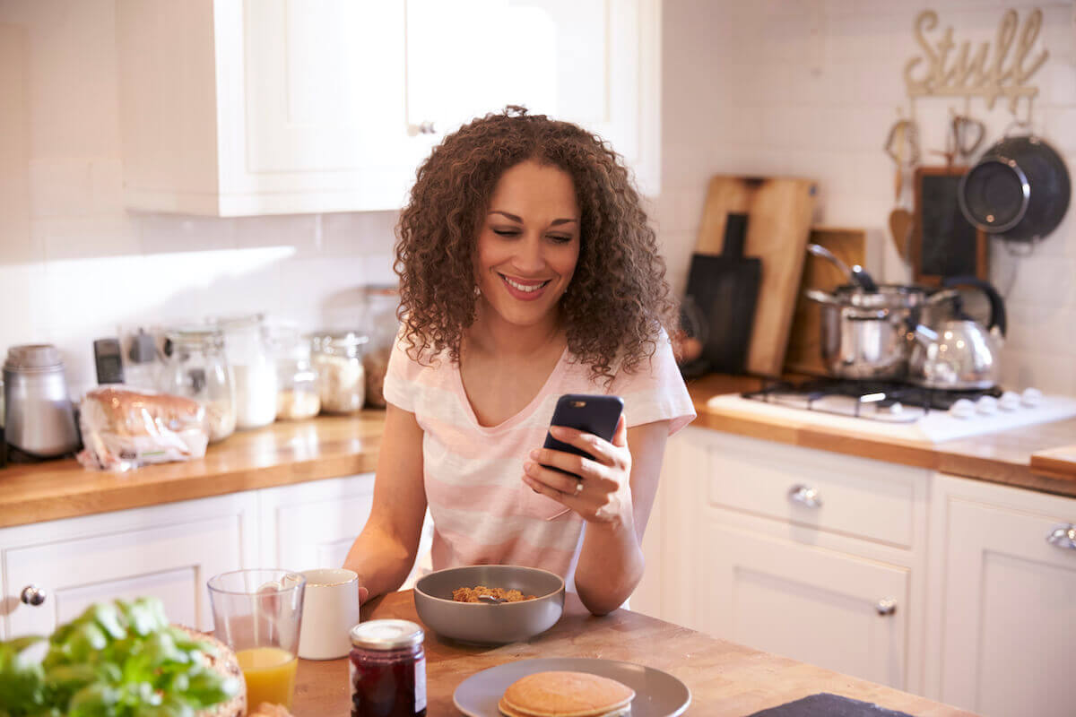 Woman in kitchen smiling while looking at smartphone-Caregiving apps