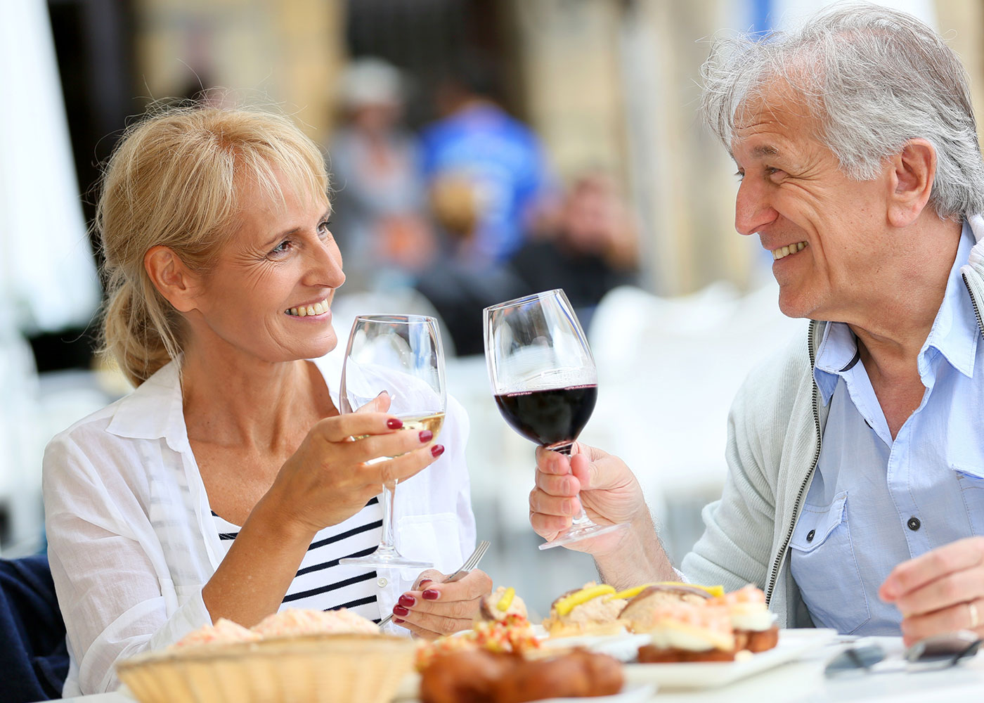 Older man and woman clinking wine glasses, eating, smiling at each other-Dining at HarborChase