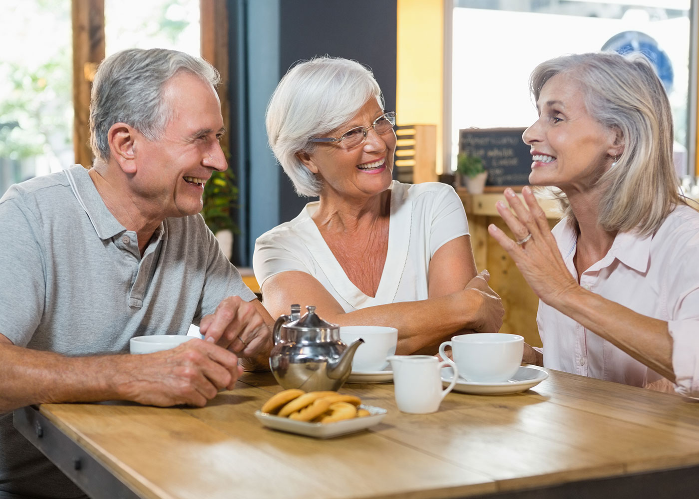 Older male with two older females; sitting at cafe table with coffee; talking and smiling at each other