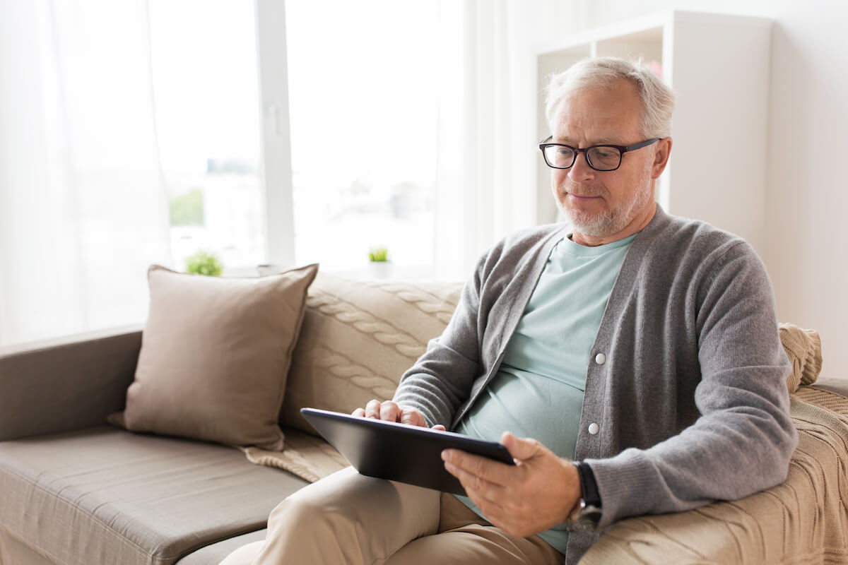 senior-man-with-tablet-pc-sitting-on-sofa-at-home-HarborChase Senior Living
